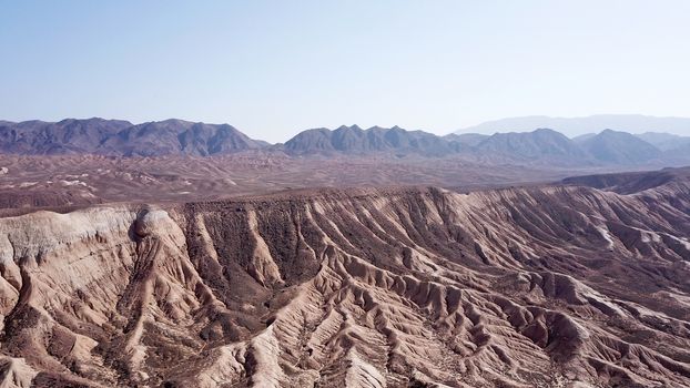 Stony hills of dark color in the steppe. Top view from the drone of rocks, dry bushes, road and gorge. Bright Sunny day and blue sky. A desolate area, the land dried up. Steppes Of Kazakhstan.