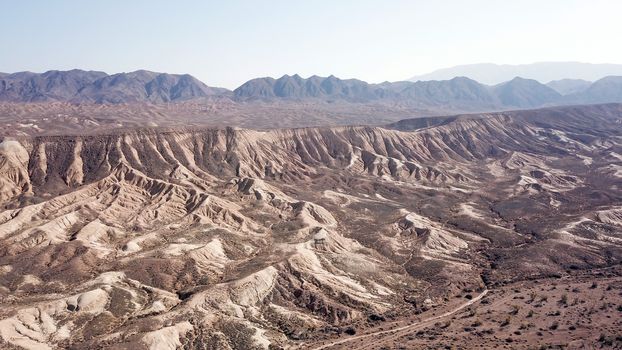 Colored hills of the gorge in the desert. Top view from drone of the red-orange-yellow hills. Cut in different layers, like epochs. Clay of the mountain. Low dry bushes, cracks, blue sky. Kazakhstan.