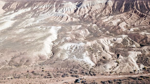 Colored hills of the gorge in the desert. Top view from drone of the red-orange-yellow hills. Cut in different layers, like epochs. Clay of the mountain. Low dry bushes, cracks, blue sky. Kazakhstan.