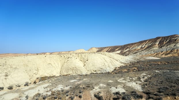 Colored hills of the gorge in the desert. Top view from drone of the red-orange-yellow hills. Cut in different layers, like epochs. Clay of the mountain. Low dry bushes, cracks, blue sky. Kazakhstan.