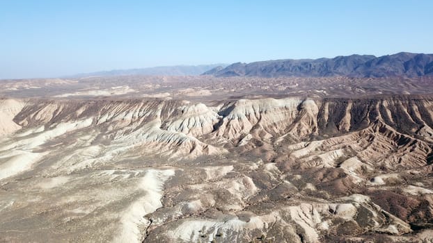 Colored hills of the gorge in the desert. Top view from drone of the red-orange-yellow hills. Cut in different layers, like epochs. Clay of the mountain. Low dry bushes, cracks, blue sky. Kazakhstan.