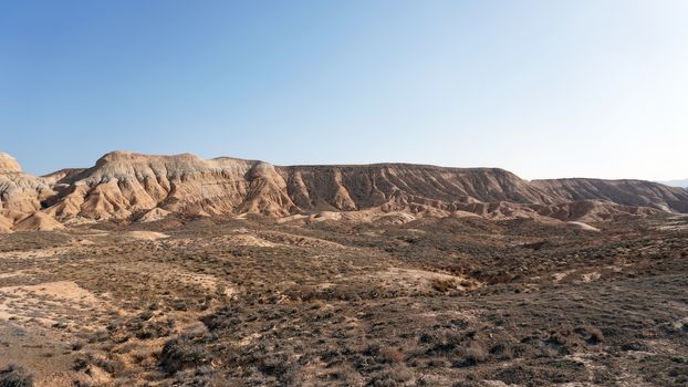 Colored hills of the gorge in the desert. Top view from drone of the red-orange-yellow hills. Cut in different layers, like epochs. Clay of the mountain. Low dry bushes, cracks, blue sky. Kazakhstan.