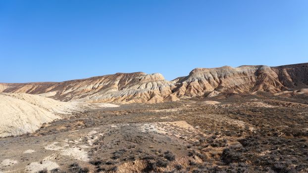 Colored hills of the gorge in the desert. Top view from drone of the red-orange-yellow hills. Cut in different layers, like epochs. Clay of the mountain. Low dry bushes, cracks, blue sky. Kazakhstan.