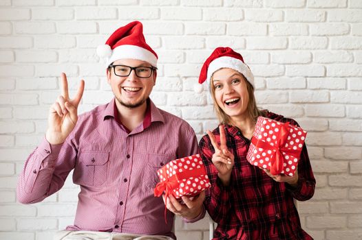 Happy christmas couple in santa hats holding gift boxes on white brick wall background