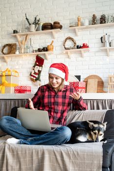 Chhristmas online greetings. Happy young woman in santa hat greeting her friends in video chat or call on laptop