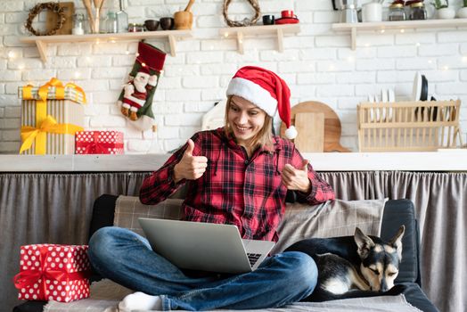 Chhristmas online greetings. Happy young woman in santa hat greeting her friends in video call on laptop showing thumbs up