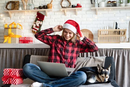 Chhristmas online greetings. Happy young woman in santa hat greeting her friends in video call on laptop showing christmas gift