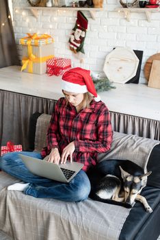 Chhristmas online greetings. young blond woman in santa hat working on laptop sitting on the couch