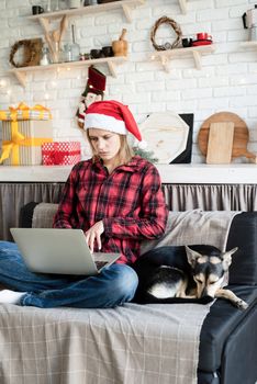 Chhristmas online greetings. young blond woman in santa hat working on laptop sitting on the couch