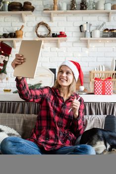 Christmas online greetings. young blond woman in santa hat working on tablet sitting on the couch