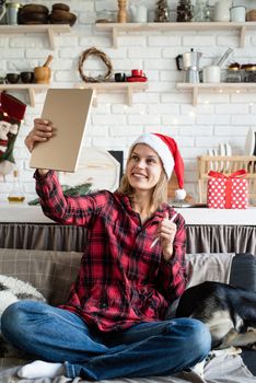 Christmas online greetings. young blond woman in santa hat working on tablet sitting on the couch