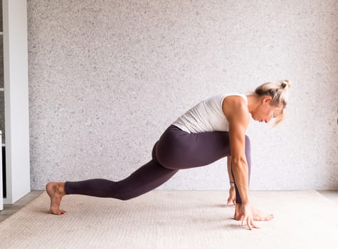 Healthy lifestyle. Young attractive woman practicing yoga, wearing sportswear, white shirt and purple pants, indoor full length, gray background