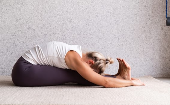 Healthy lifestyle. Young attractive woman practicing yoga, wearing sportswear, white shirt and purple pants, indoor full length, gray background