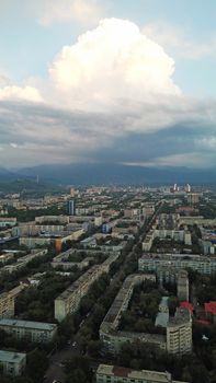 Huge clouds over the city of Almaty. Clouds hang near the mountains. Sunset. You can see different buildings, mosques, churches, and parks. Everything is illuminated by the red rays of the sun.