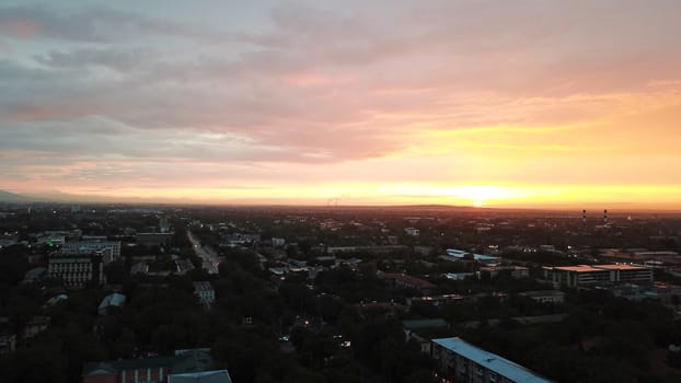 Red sunset over the city of Almaty. Clouds shimmer with different colors from yellow-red to blue. The city is plunged into darkness. Night falls. Lights are on, cars are driving. The view from the top