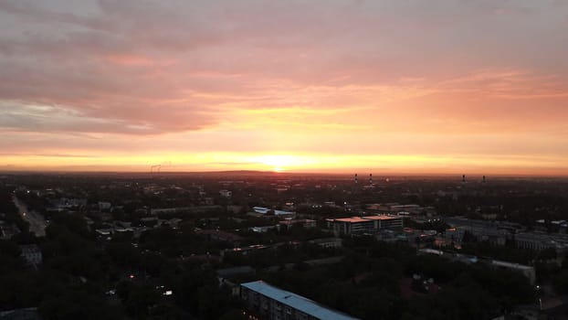 Red sunset over the city of Almaty. Clouds shimmer with different colors from yellow-red to blue. The city is plunged into darkness. Night falls. Lights are on, cars are driving. The view from the top