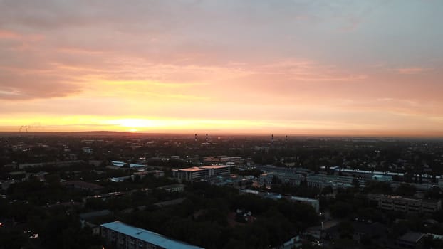 Red sunset over the city of Almaty. Clouds shimmer with different colors from yellow-red to blue. The city is plunged into darkness. Night falls. Lights are on, cars are driving. The view from the top