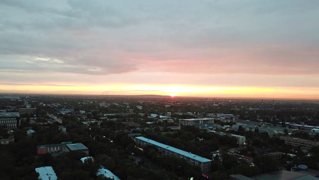 Red sunset over the city of Almaty. Clouds shimmer with different colors from yellow-red to blue. The city is plunged into darkness. Night falls. Lights are on, cars are driving. The view from the top