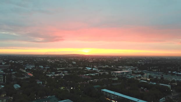 Red sunset over the city of Almaty. Clouds shimmer with different colors from yellow-red to blue. The city is plunged into darkness. Night falls. Lights are on, cars are driving. The view from the top