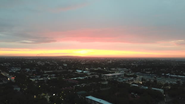 Red sunset over the city of Almaty. Clouds shimmer with different colors from yellow-red to blue. The city is plunged into darkness. Night falls. Lights are on, cars are driving. The view from the top