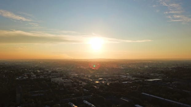 Bright color sunset over the city of Almaty. Huge clouds over the mountains and the city shimmer from bright blue to yellow and dark blue. Tall houses and green trees, cars driving on the roads.