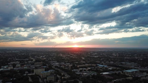 Red sunset over the city of Almaty. Clouds shimmer with different colors from yellow-red to blue. The city is plunged into darkness. Night falls. Lights are on, cars are driving. The view from the top