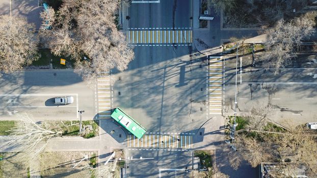 Top view of a road junction in the city of Almaty. The vehicle is waiting for the traffic light signal and is moving in its own direction. Cars, buses, and people move through the intersection.