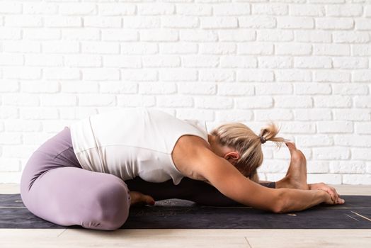 Healthy lifestyle. Young attractive woman practicing yoga, wearing sportswear, white shirt and purple pants, indoor full length, gray background