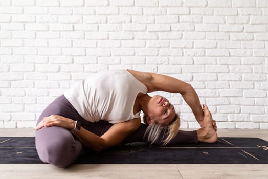 Healthy lifestyle. Young attractive woman practicing yoga, wearing sportswear, white shirt and purple pants, indoor full length, gray background