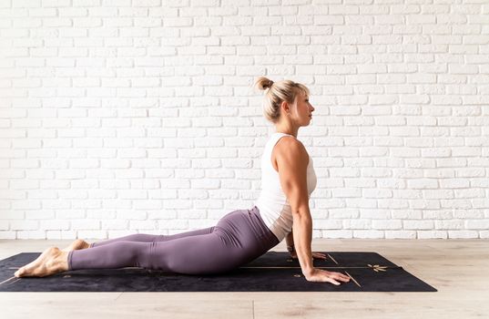 Healthy lifestyle. Young attractive woman practicing yoga, wearing sportswear, white shirt and purple pants, indoor full length, gray background