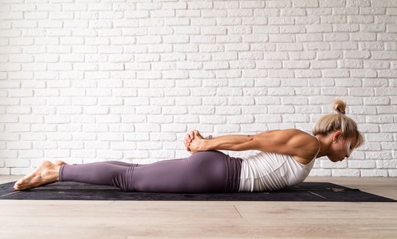 Healthy lifestyle. Young attractive woman practicing yoga, wearing sportswear, white shirt and purple pants, indoor full length, gray background