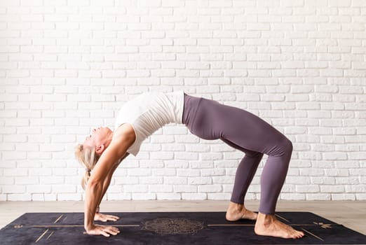 Healthy lifestyle. Young attractive woman practicing yoga, wearing sportswear, white shirt and purple pants, indoor full length, gray background