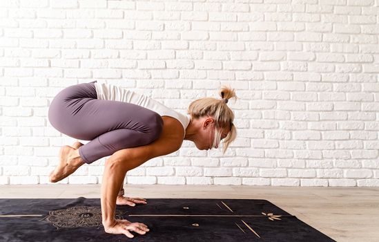 Healthy lifestyle. Young attractive woman practicing yoga, wearing sportswear, white shirt and purple pants, indoor full length, gray background