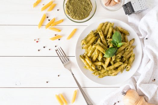 Italian cuisine. Vegan penne pasta in a basil pesto sauce top view on white wooden background flat lay