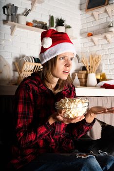 Movie night. Young woman in santa hat watching movies at home at christmas night eating popcorn