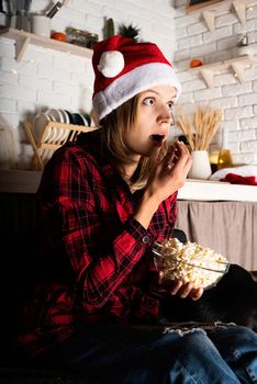Movie night. Young woman in santa hat watching movies at home at christmas night eating popcorn