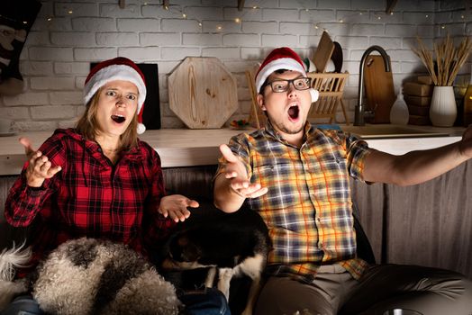 Movie night. Young couple watching movies at home at christmas pointing to the screen eating popcorn