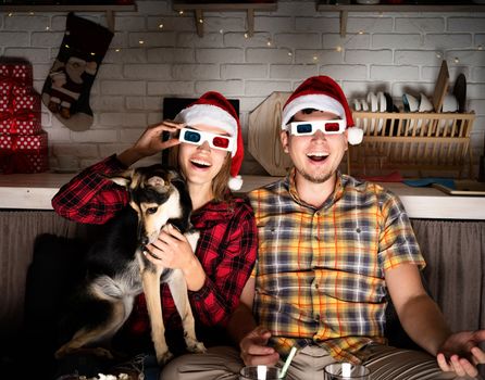 Movie night. Young couple in 3D glasses watching movies at home at christmas pointing to the screen eating popcorn