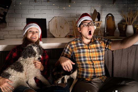 Movie night. Young couple showing surprise watching movies at home at christmas