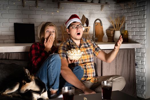 Movie night. Young couple showing surprise watching movies at home at christmas