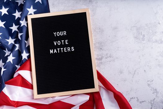 Black letter board with the text your vote matters with American flag on white marble background