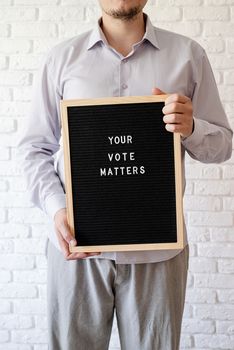 voting concept. Man holding letterboard with the words your vote matters on white brick background