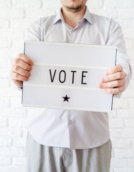 voting concept. Man holding lightbox with the word Vote on white brick background