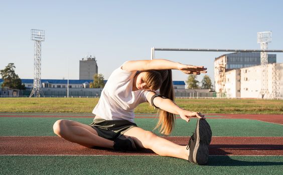 Fitness and sports. Teenager girl doing stretching at the stadium