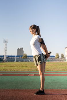 Fitness and sports. Teenager girl stretching her legs at the stadium