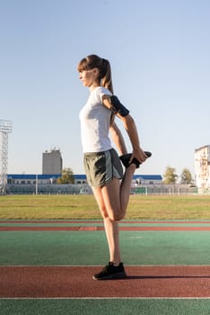 Fitness and sports. Teenager girl stretching her legs at the stadium