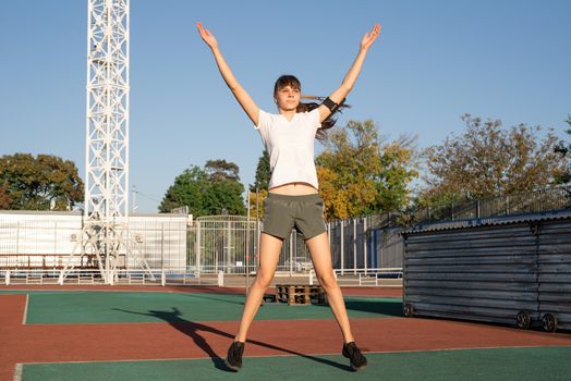 Healthy lifestyle concept. Sport and fitness. Teenager girl doing jumping jacks or star jumps at the stadium