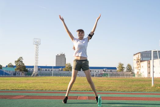 Healthy lifestyle concept. Sport and fitness. Teenager girl doing jumping jacks or star jumps at the stadium