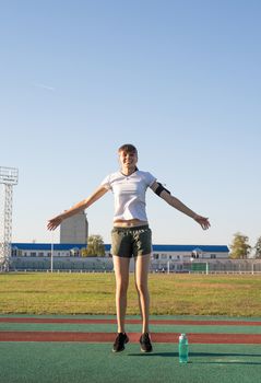 Healthy lifestyle concept. Sport and fitness. Teenager girl doing jumping jacks or star jumps at the stadium