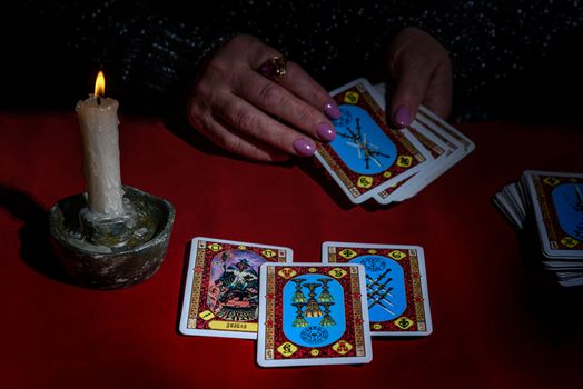 A woman reads Tarot cards by candlelight on a red table